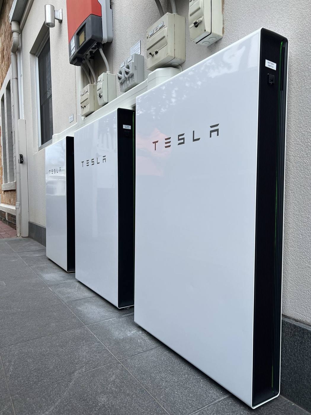 Three Tesla Powerwall batteries installed side by side on a rendered wall