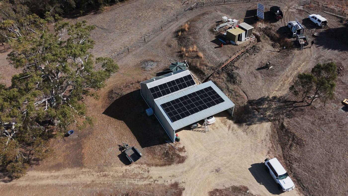 Aerial of an off-grid property with a shed solar array, ground-mounted panels and work vehicles