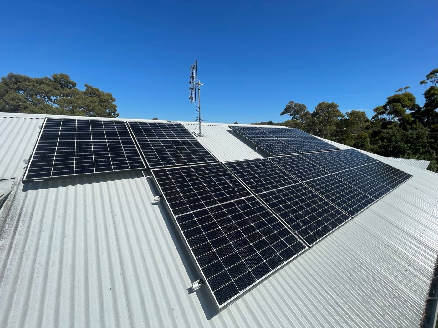 Solar panels installed on a silver corrugated roof under a clear blue sky