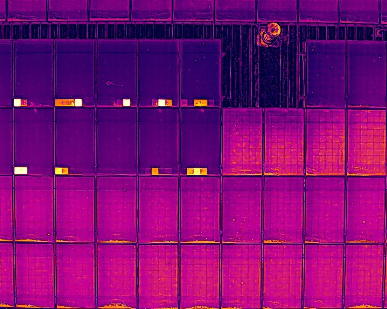 Thermal drone image of solar panels with bright hot spots where dirt has overheated the cells