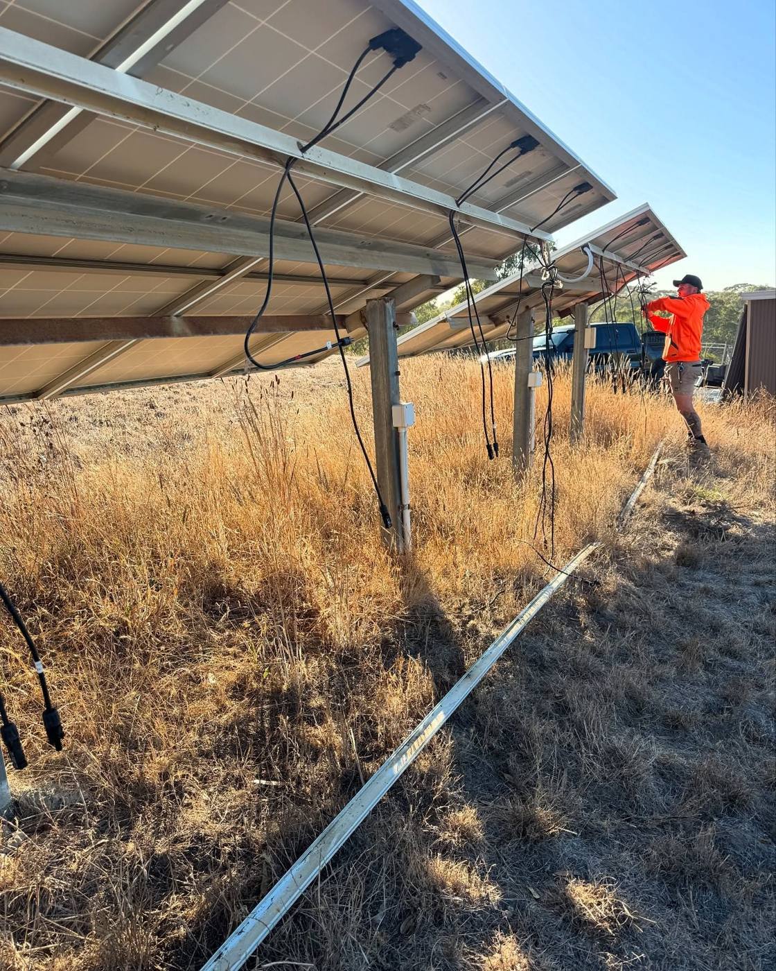 Electrician wiring a ground-mounted solar array in dry grass