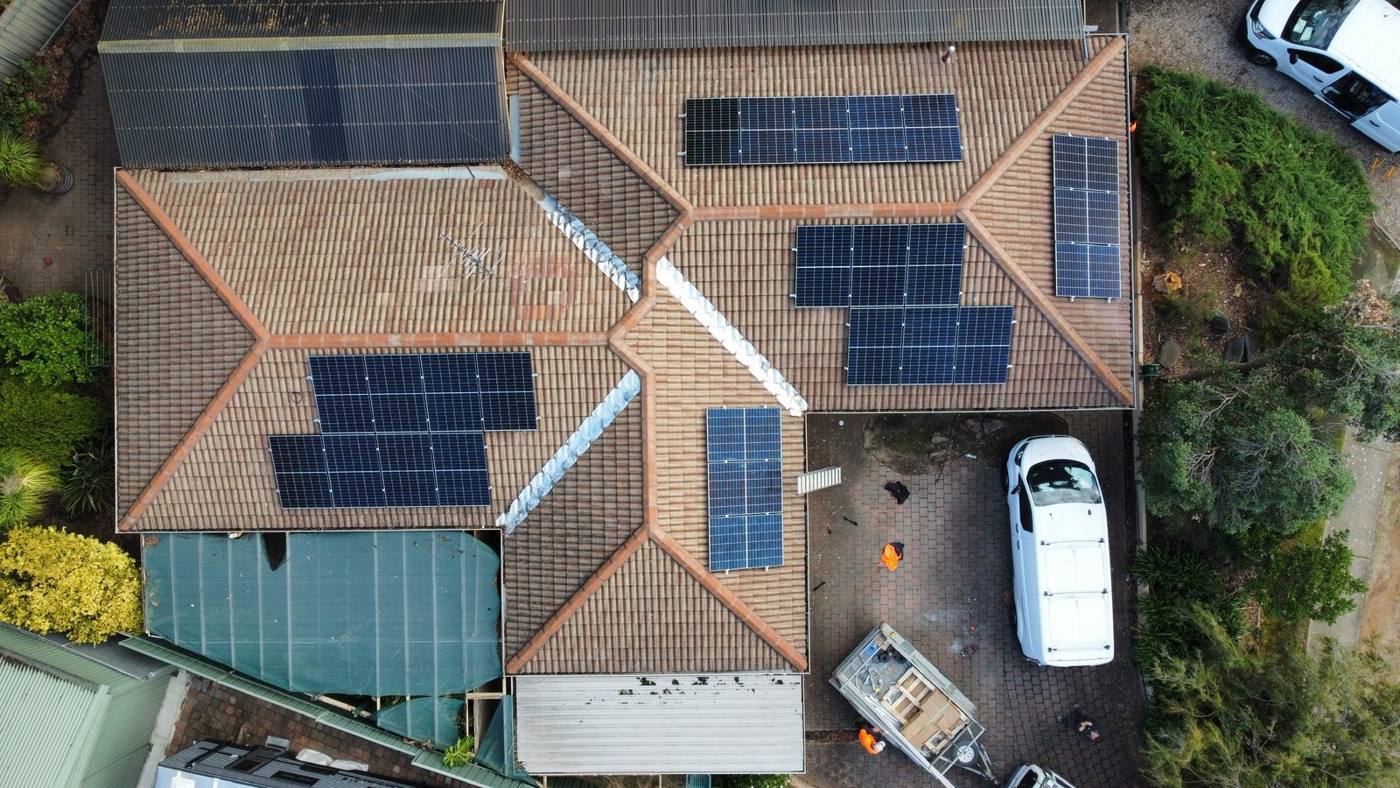 Drone view of solar arrays across several faces of a tiled roof, with the NG Elec van in the driveway